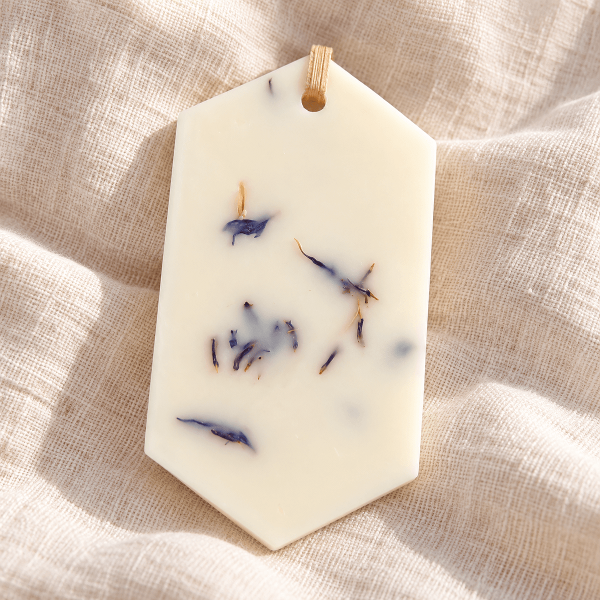 Odorizant pentru dulap din ceară naturală, decorat cu flori uscate albastre, cu parfum de zambile și așezat pe o pânză textilă ivory.